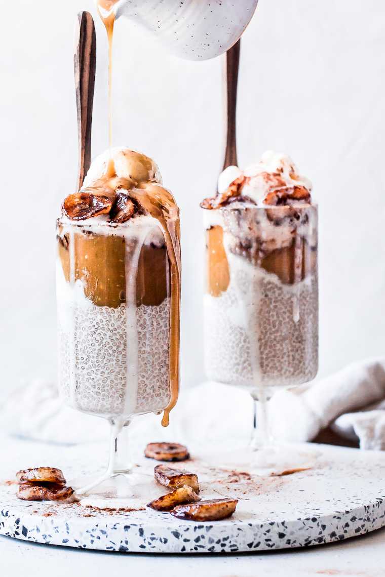 two glasses with chia pudding, vegan caramel and bananas on which sweet sauce in being poured