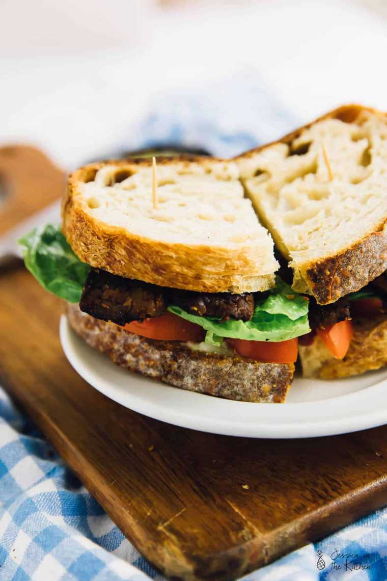 white plate with a halved tempeh lettuce and tomato sandwich