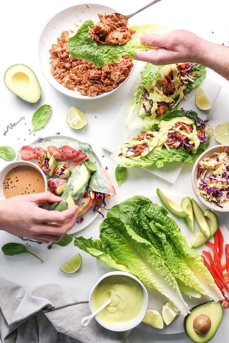 top view of white table full of vegetables such as romaine lettuce, lime, avocado and red bell pepper to make vegan wraps