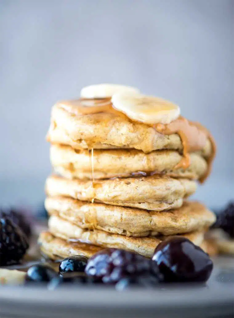 six vegan quinoa flour pancakes stacked on top of each other with peanut butter and fruit