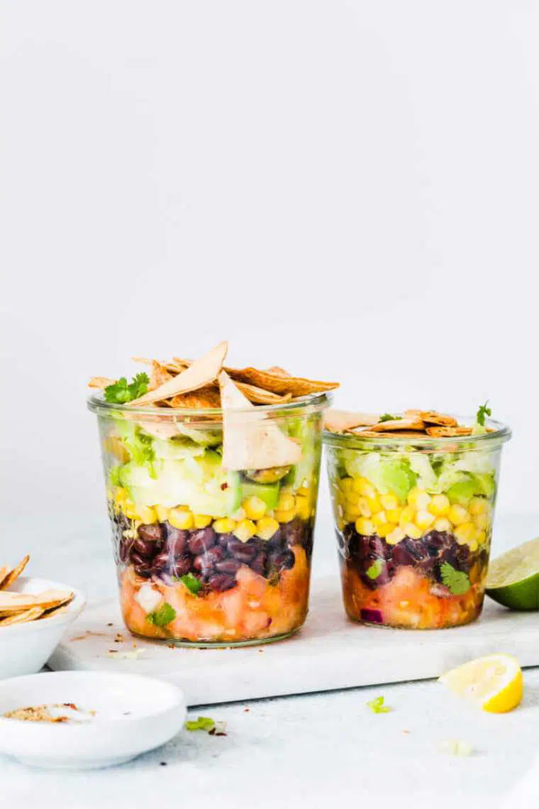 two glass jars with layered vegan mexican salad and tortillas