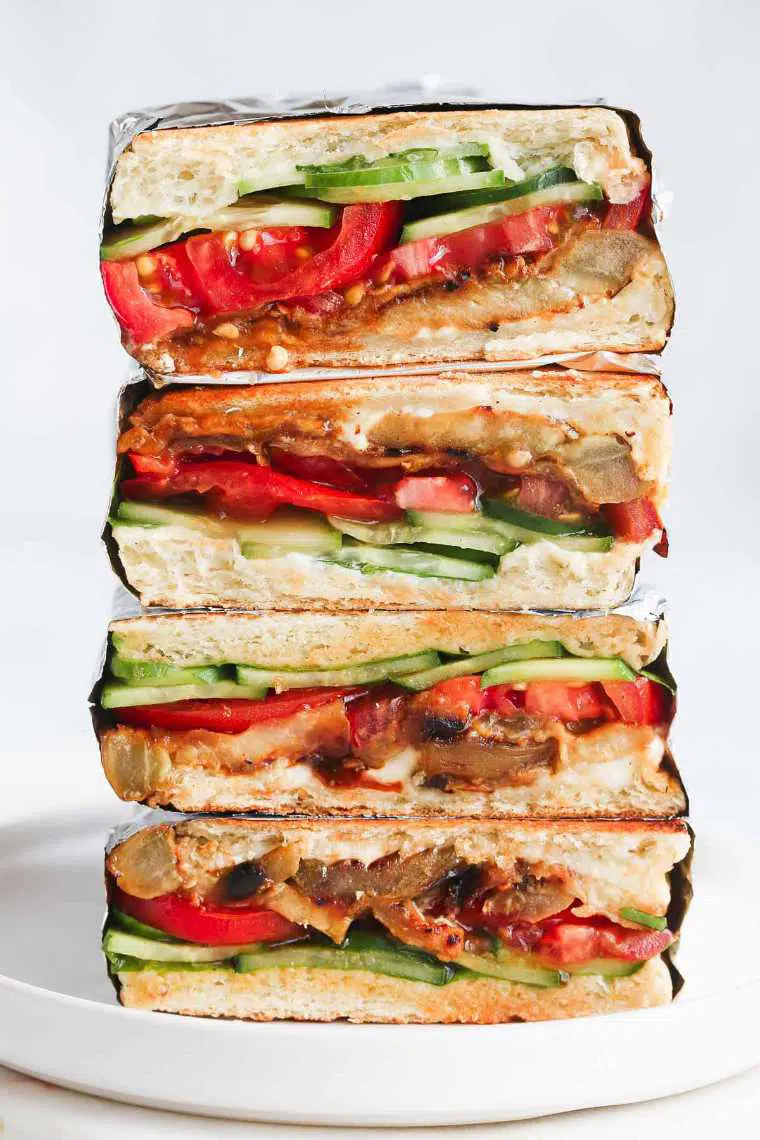 four vegan eggplant sandwiches with tomato and cucumber on top of each other as one of the best cold lunch ideas