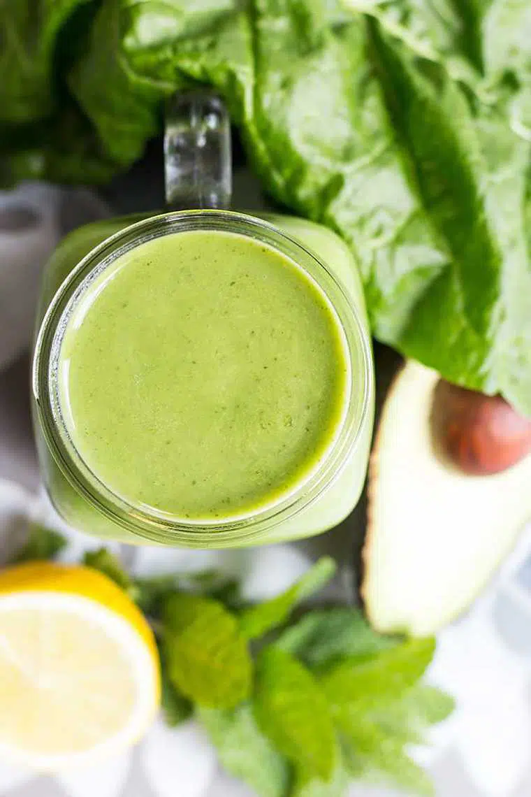 table with leafy greens, avocado, mint, lemon and a glass of green superfood smoothie
