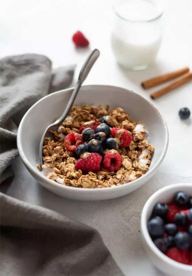 white bowl of homemade almond butter granola with berries and a spoon