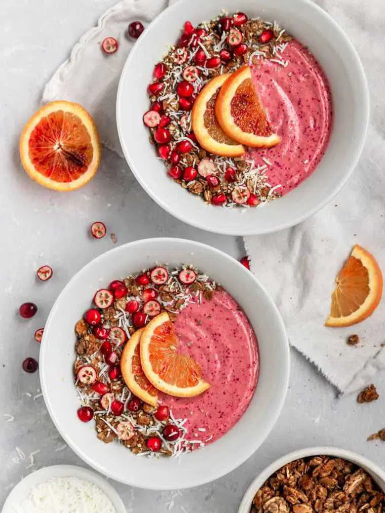 white table with blood oranges, cranberries and two pink smoothie bowls topped with superfoods