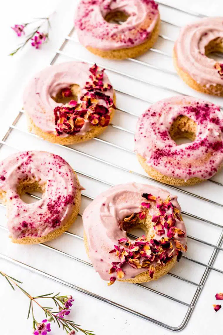 cooling rack on a table with six vibrantly pink vegan cake doughnuts topped with rose petals
