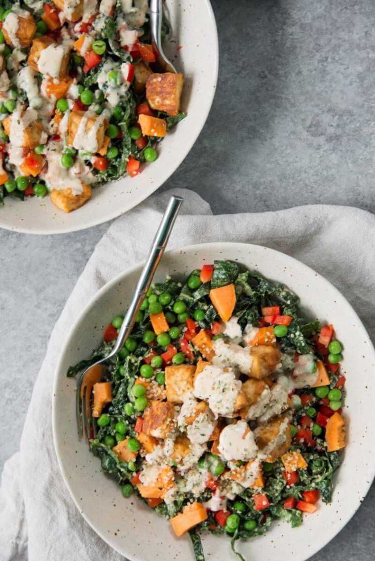 two white bowls on a table with peas, carrots, tofu, kale and vegan sauce