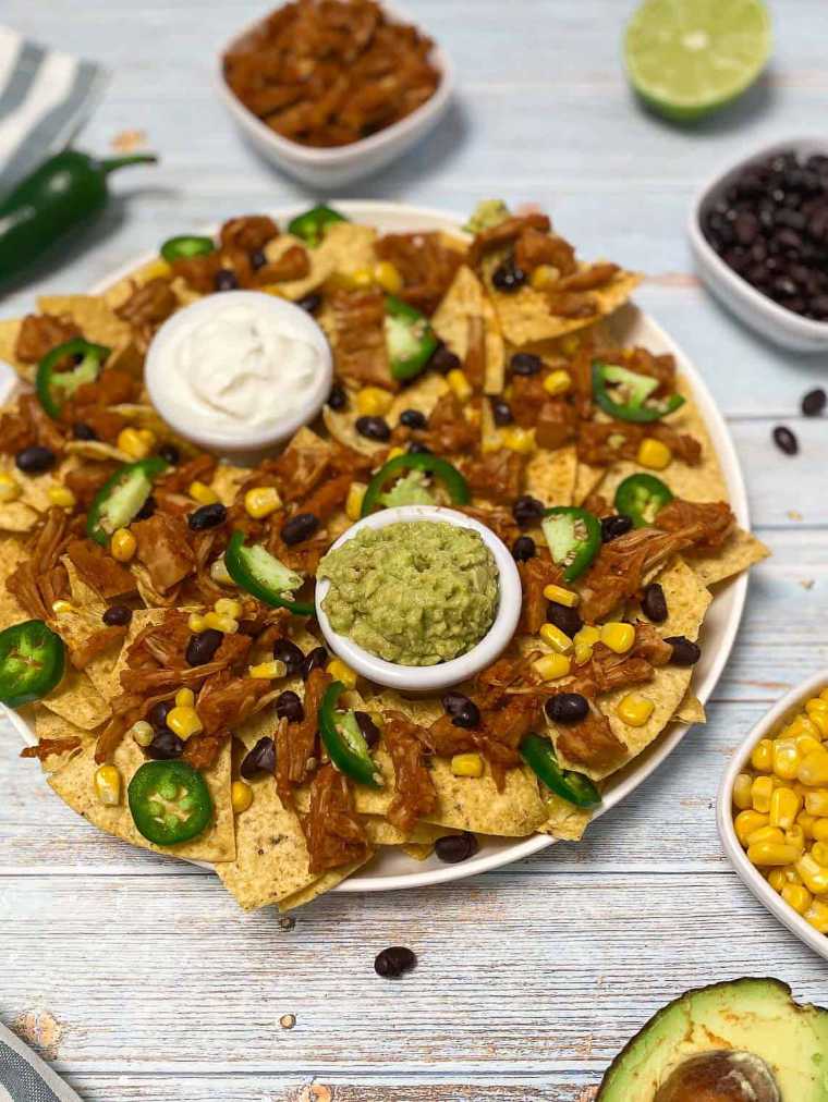 wooden table with a white plate of Pulled Jackfruit Nachos with dips