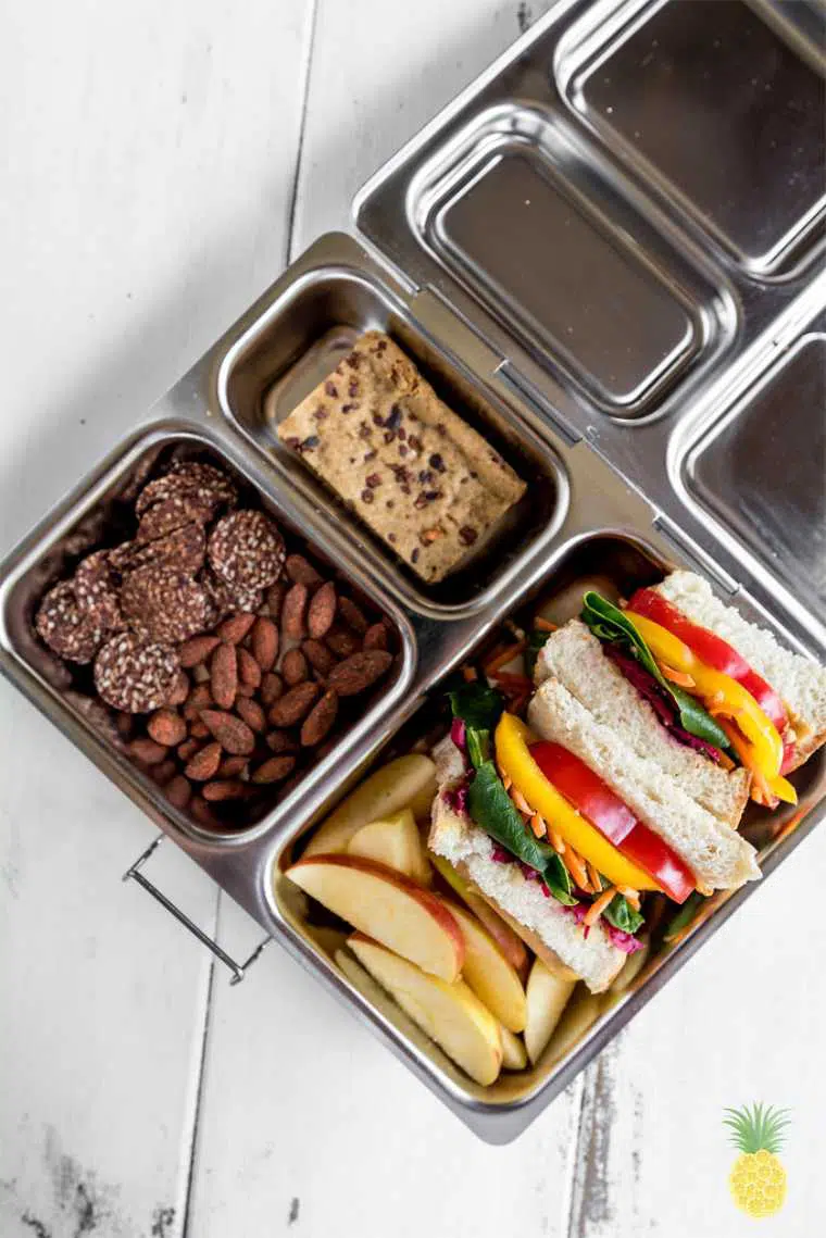 metal lunchbox containing almonds, energy balls, apple slices and a homemade rainbow veggie sandwich