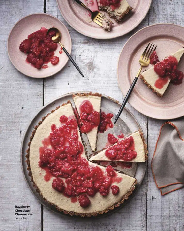 top view of a wooden table with a plate of homemade no-bake vegan cheese cake topped with raspberries and several slices taken out