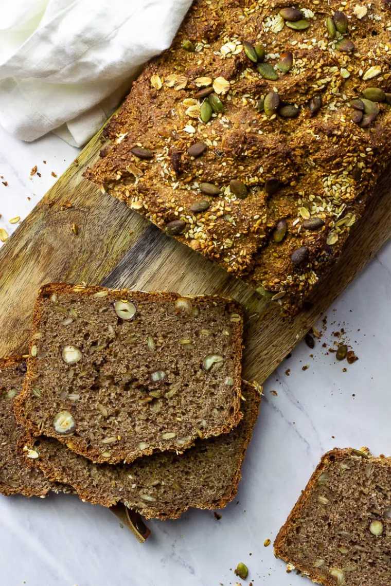 chopping board with a loaf of vegan whole gran bread with nuts and seeds