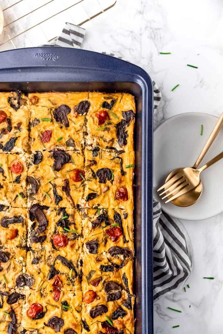 White table with a black sheet pan featuring homemade vegan vegetable frittata