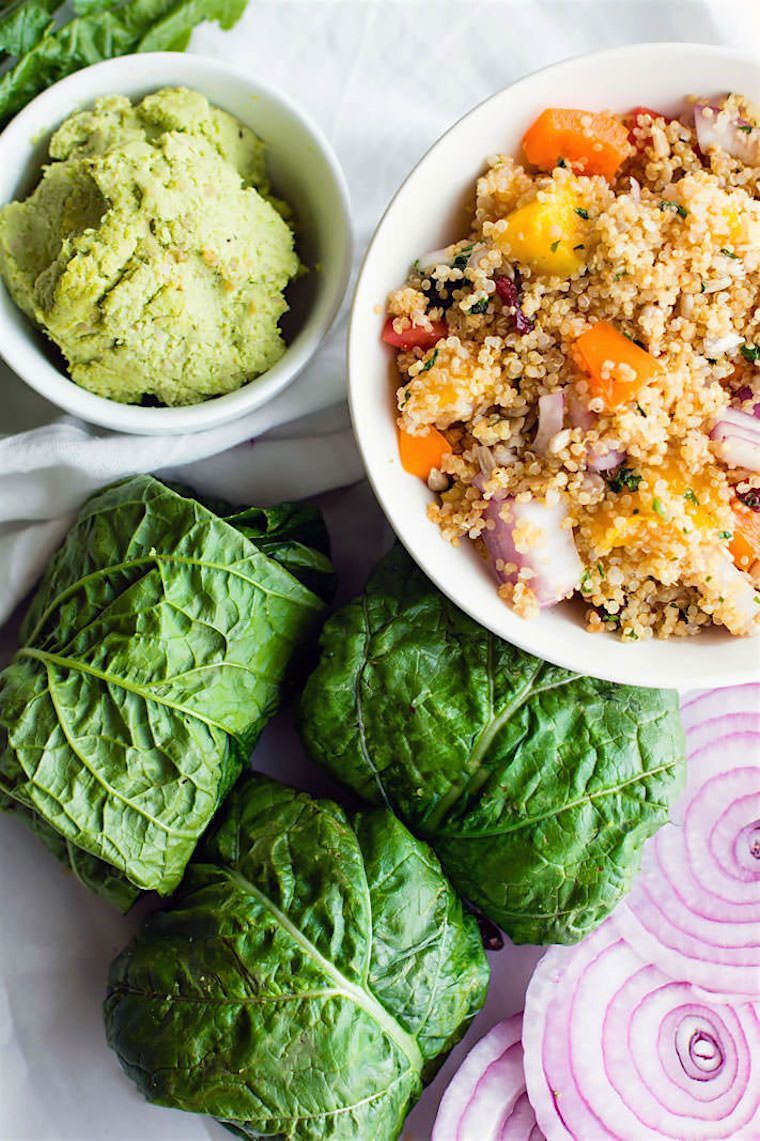 white table with a bowl of quinoa salad next to sliced red onions, edamame pesto and collard greens