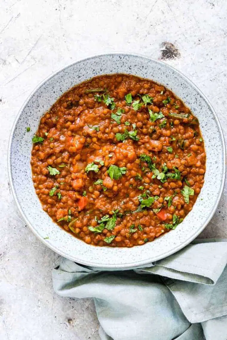 white speckled bowl with plant-based instant pot lentil soup and fresh herbs