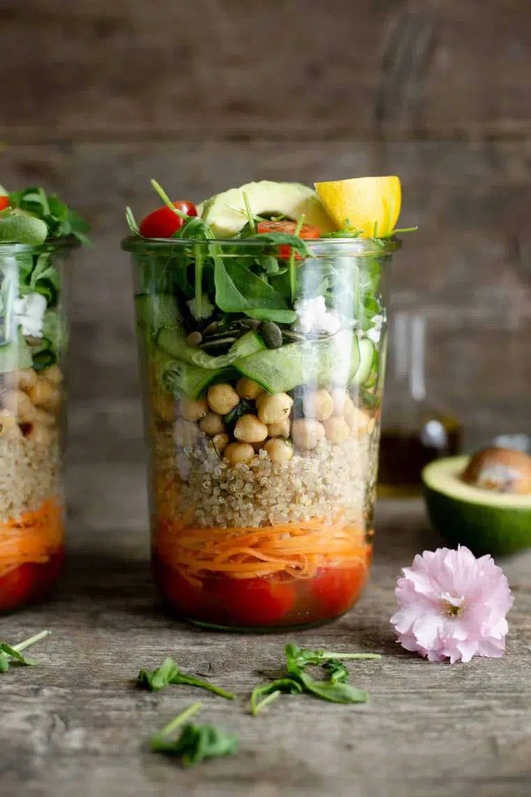 wooden table with a mason jar containing layered portable chickpea and quinoa salad