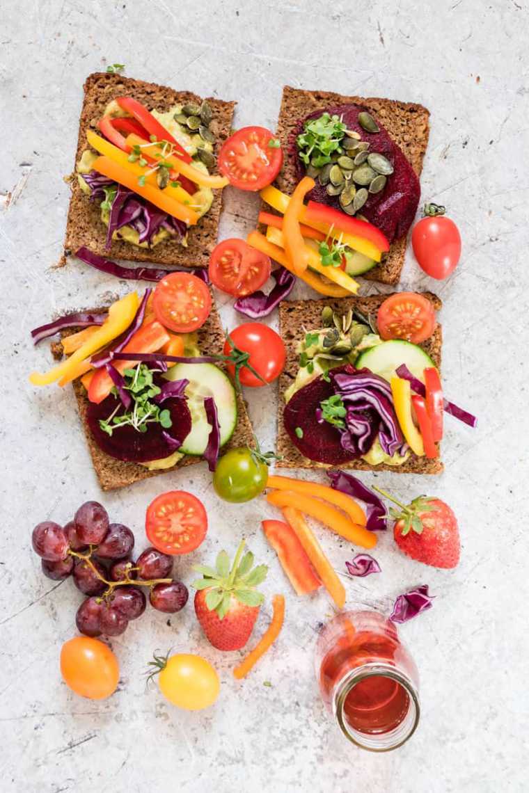 table with four slices of bread, red cabbage, beetroot, tomato bell pepper, sprouts and seeds