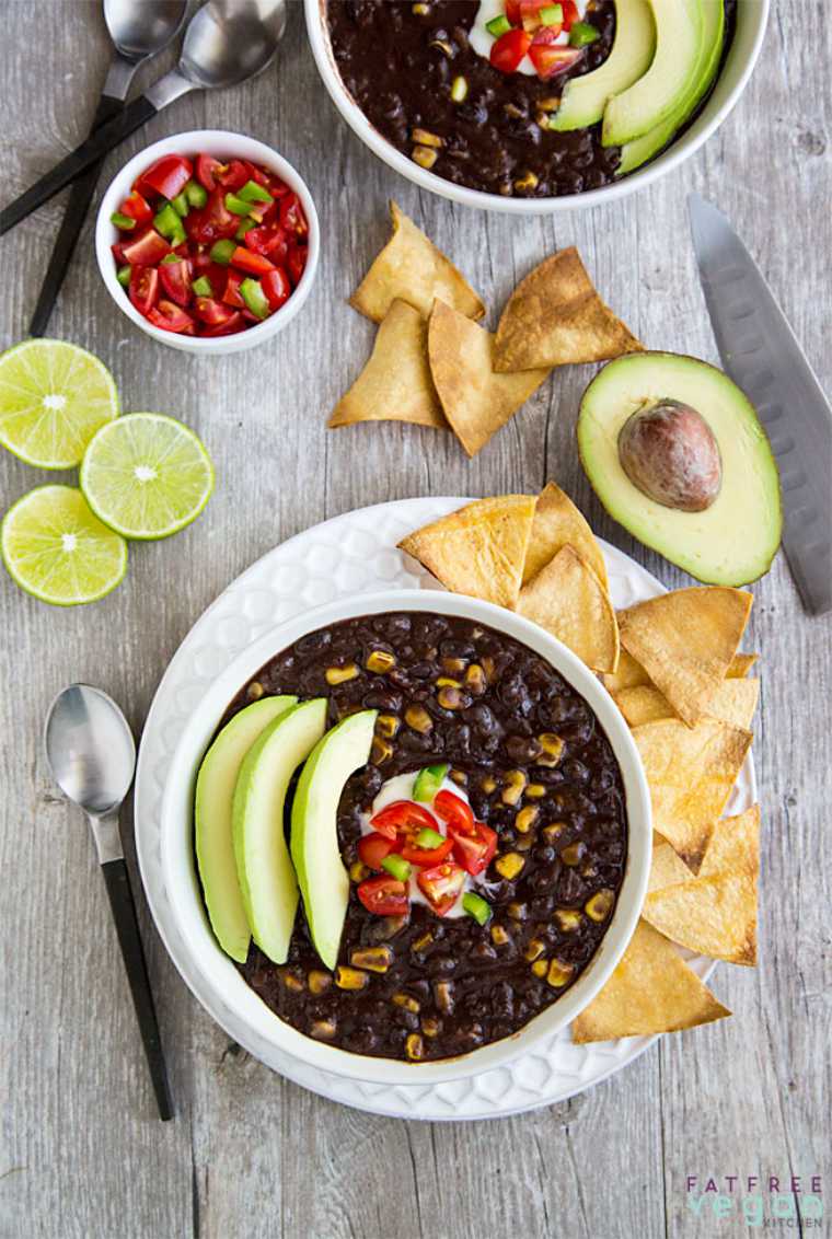 wooden table with two white bowls filled with black beans soup and sliced avocado