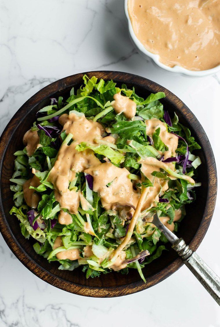 wooden bowl with chopped leafy greens that are drenched in vegan oil-free thousand island dressing