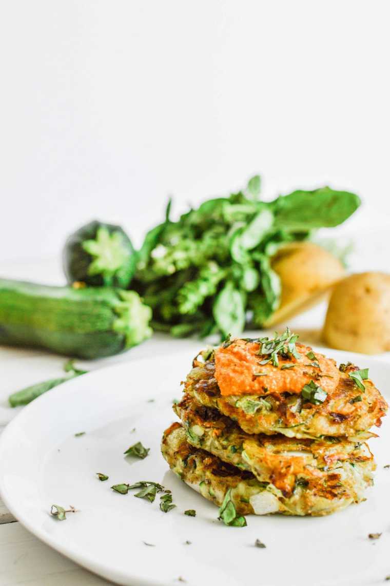 white plate with three zucchini potato fritters on top of each other next to the ingredients
