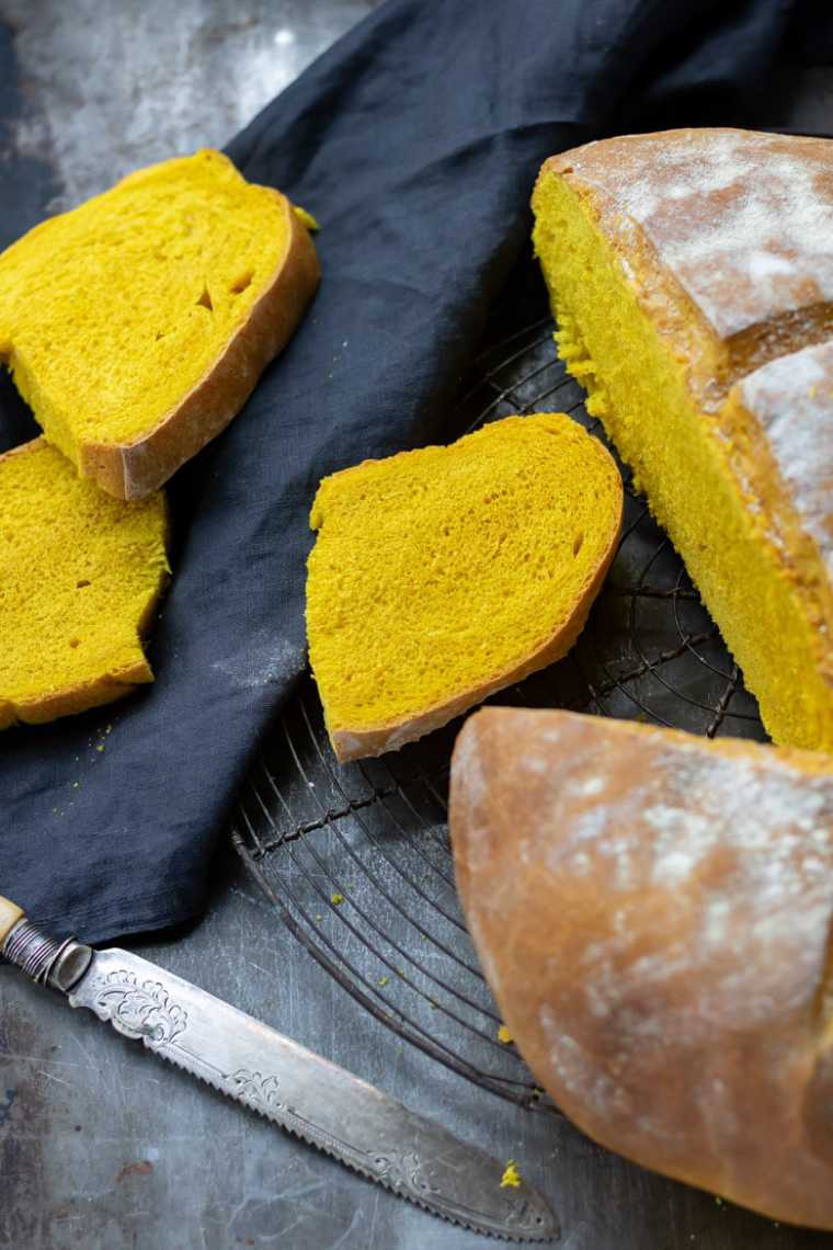 dark table with slices of yellow turmeric bread next to the whole loaf