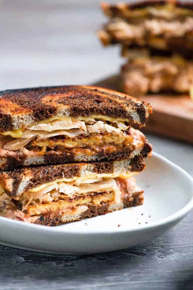 white plate with two vegan tempeh reuben sandwiches on top of each other