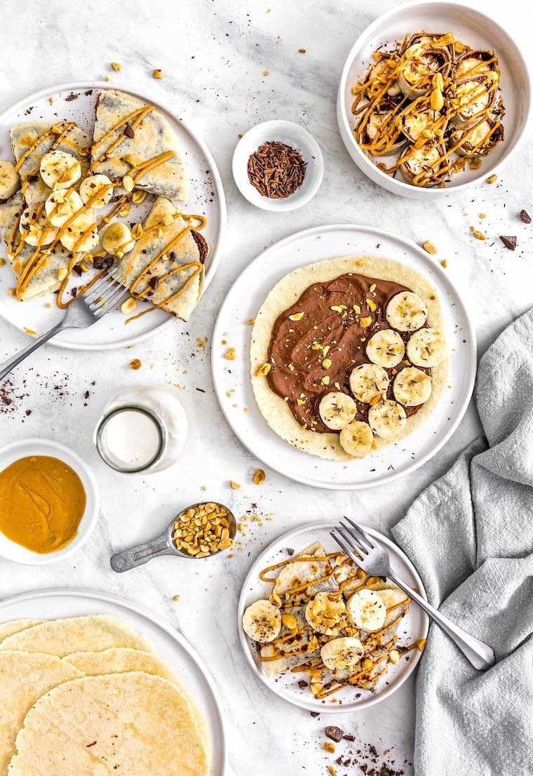 white table with different plates filled with homemade vegan sweet wraps topped with chocolate spread, peanut butter and sliced banana