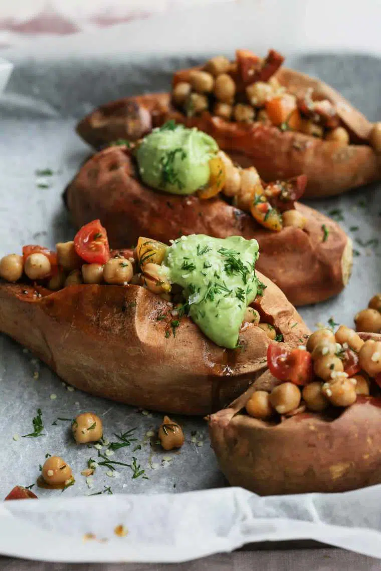 baking dish with 4 baked sweet potatoes that are stuffed with chickpeas, tomatoes and avocado cream