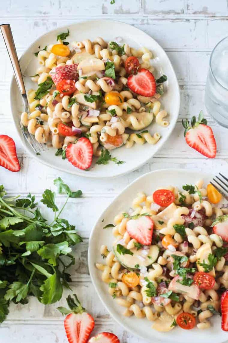 two plates with vegan pasta salad featuring tomato, strawberries and fresh herbs