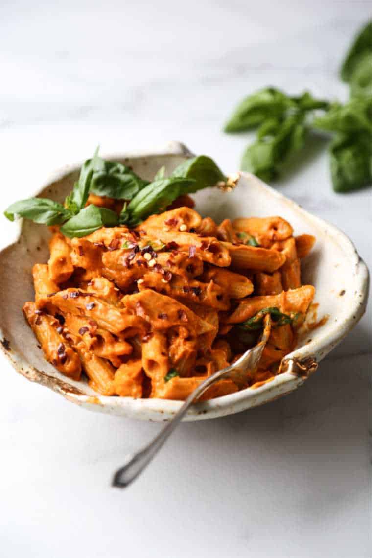 white plate with creamy red vegan penne alla vodka and basil
