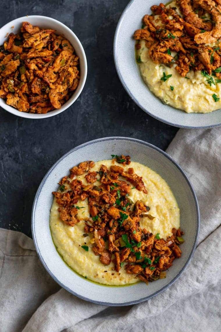 two white bowls filled with homemade vegan grits which are topped with cajun flavored soy curls
