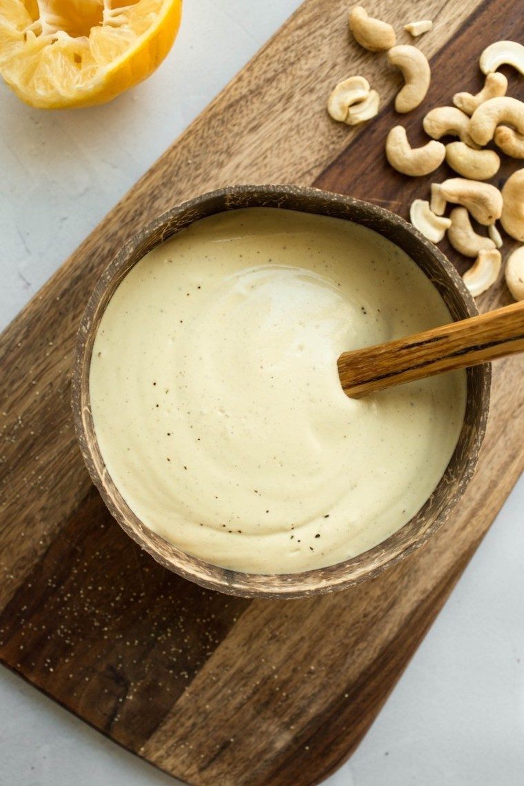 wooden chopping board with a small wooden bowl containing creamy vegan caesar dressing and some cashews on the side