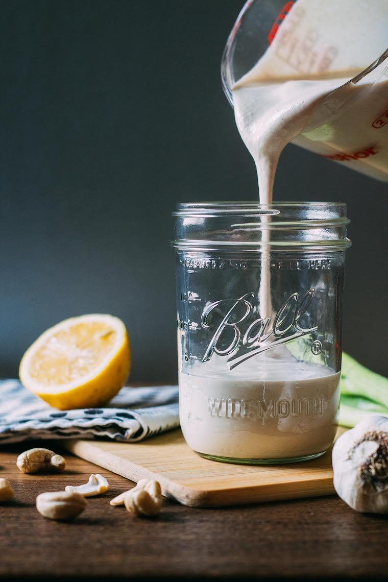 white mason jar on a wooden table in which vegan blue cheese dressing is being poured