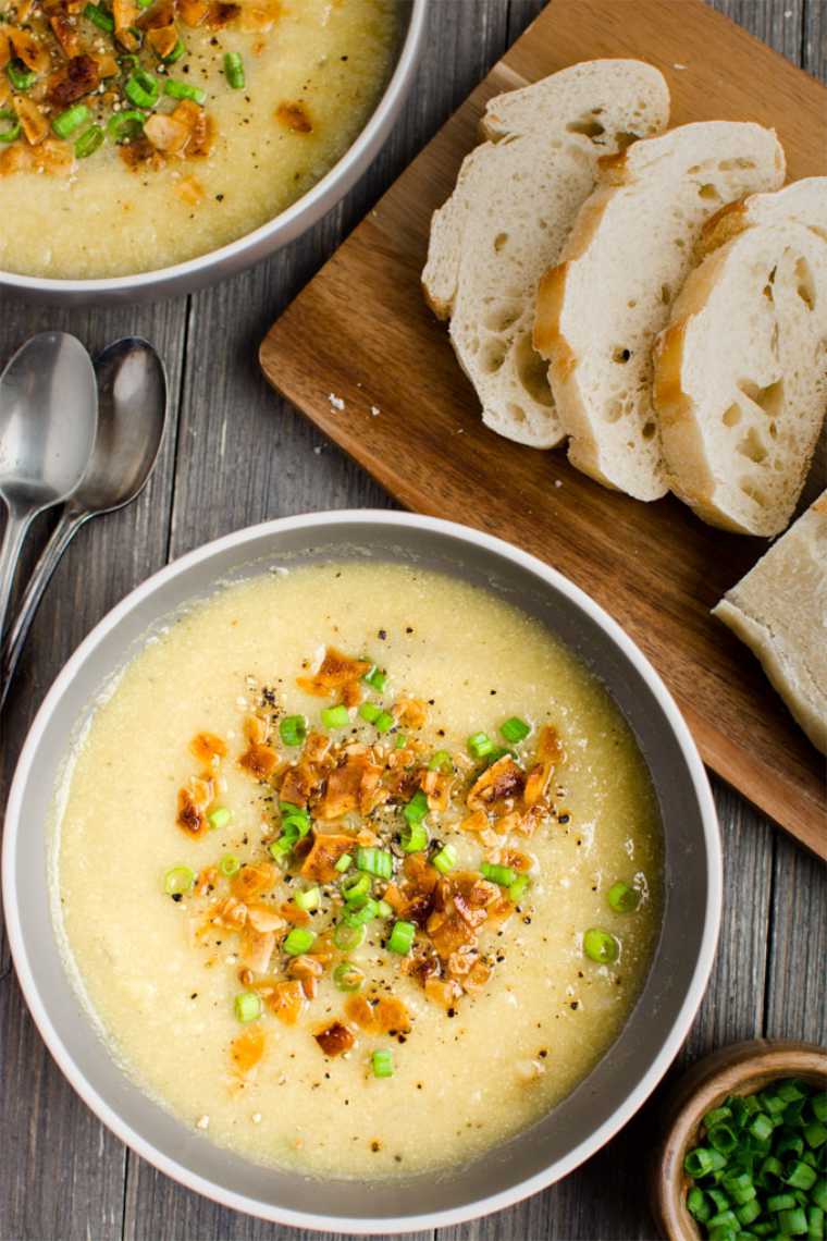 wooden table with sliced bread and two bowls of creamy cauliflower leek soup