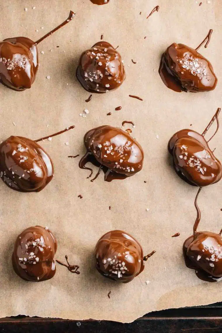 brown parchment paper with four chocolate-covered dates sprinkled with salt