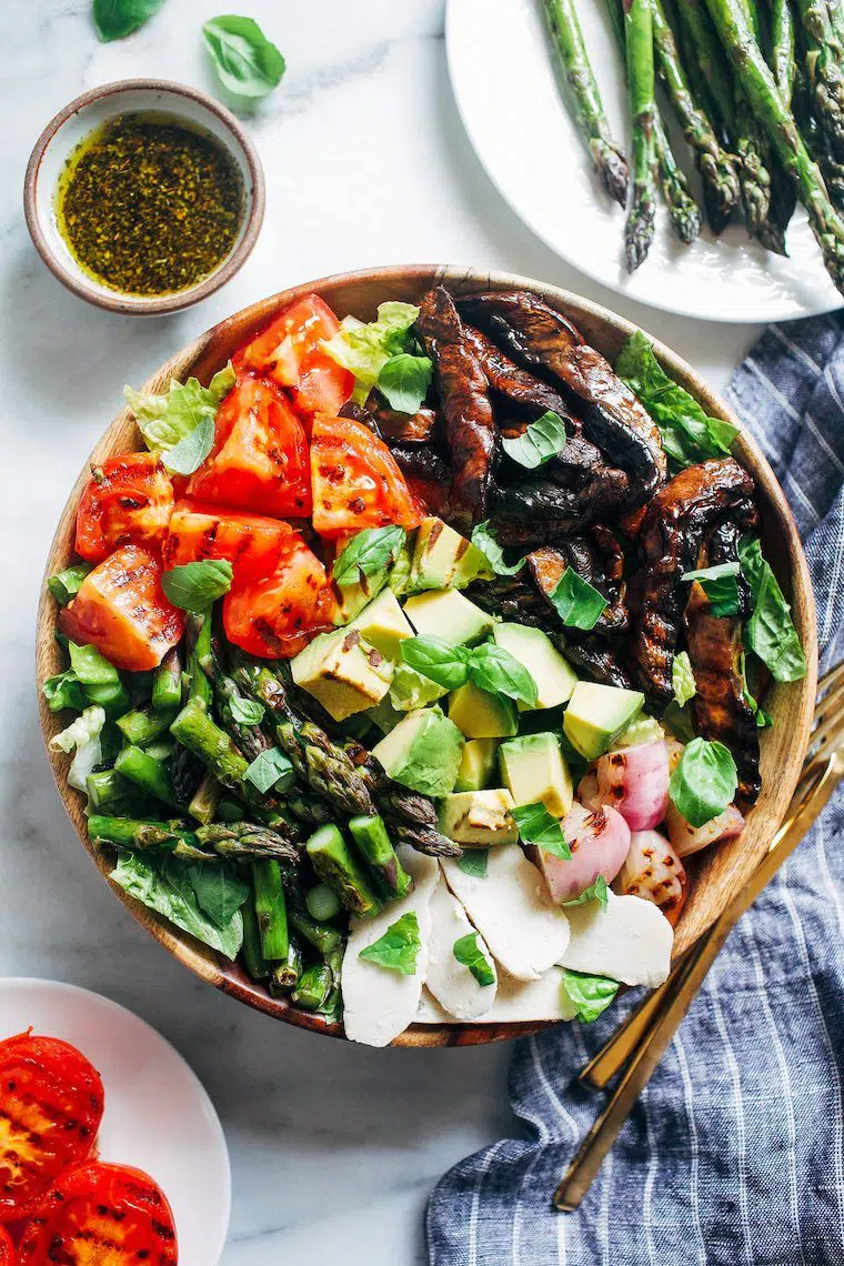 wooden bowl with leafy greens, grilled mushrooms, asparagus, tomato, avocado and vegan feta at a BBQ