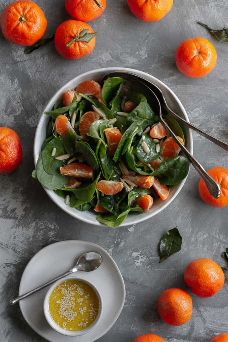 grey table with lots of mandarin and white bowl of homemade spinach mandarin orange salad
