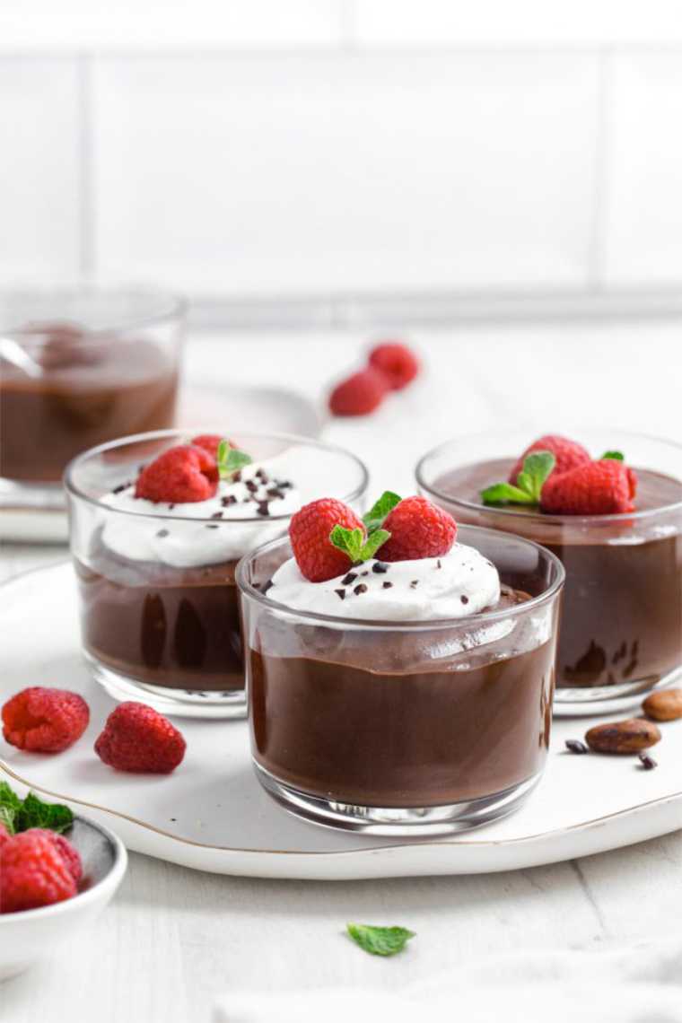 white table with four serving glasses of creamy brown chia pudding topped with fresh berries