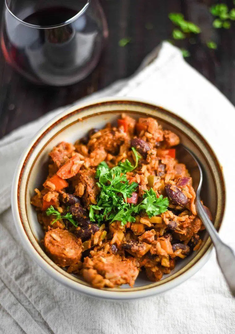 glass of red wine and a linen towel on which a bowl of hearty vegan jambalaya is placed