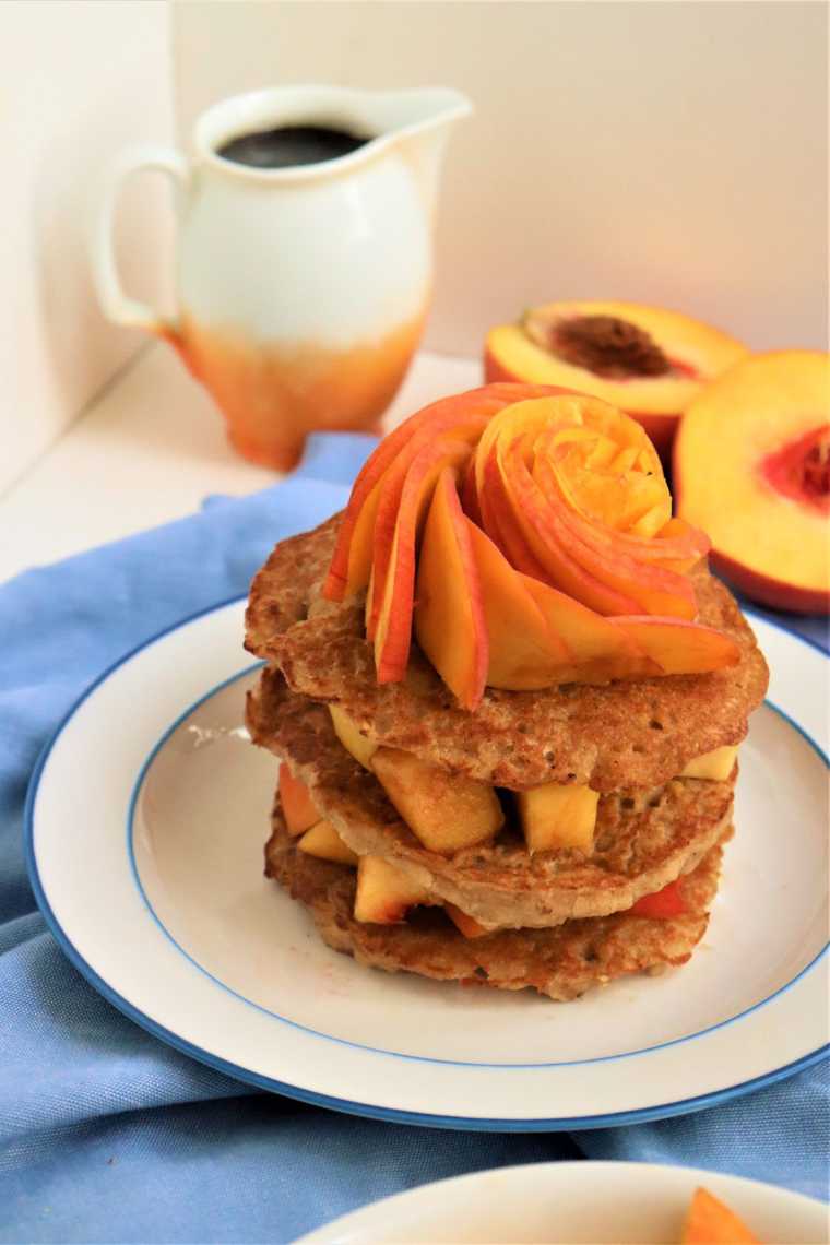 table with halved peaches and a plate with three oat pancakes layered and topped with more peaches
