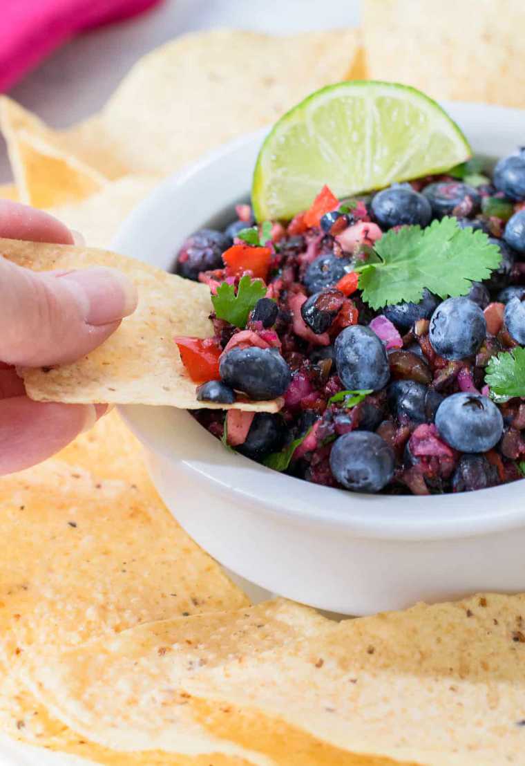 close up of a hand putting a tortilla chip into Fresh Blueberry Salsa