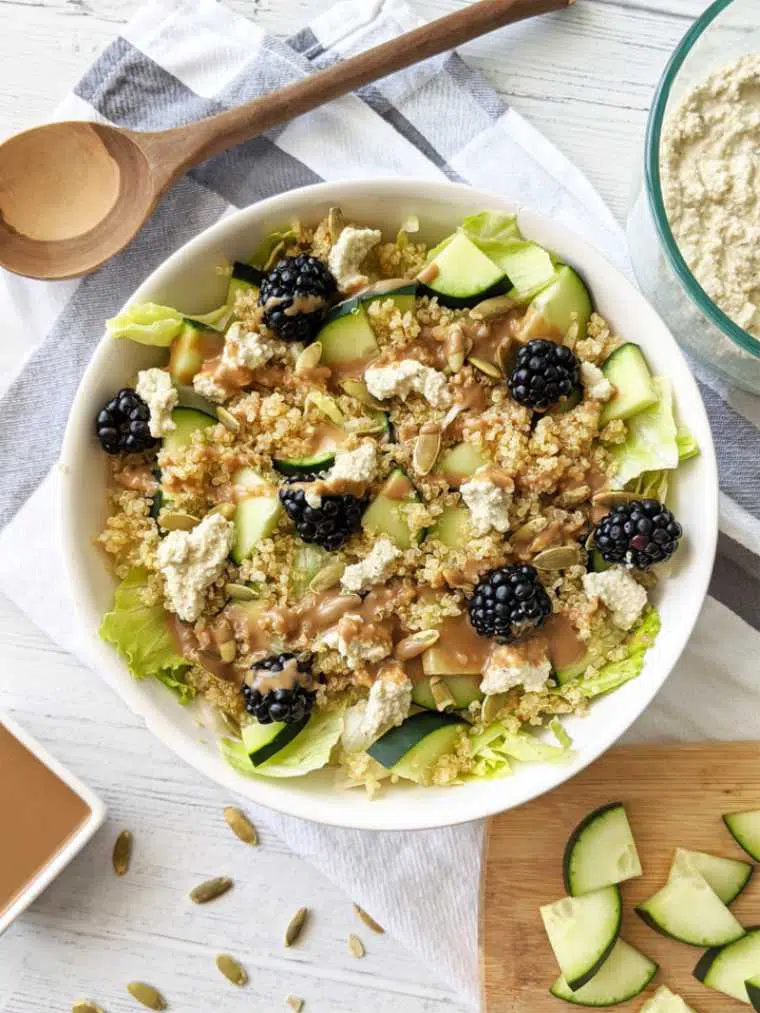large white bowl with lettuce, cucumber, quinoa, blackberries and vegan ricotta