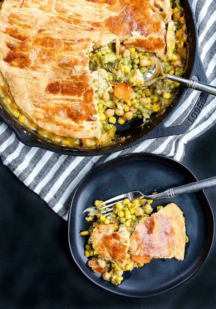 black baking dish filled with some hearty vegan pot pie with a serving taken out and put on a black plate
