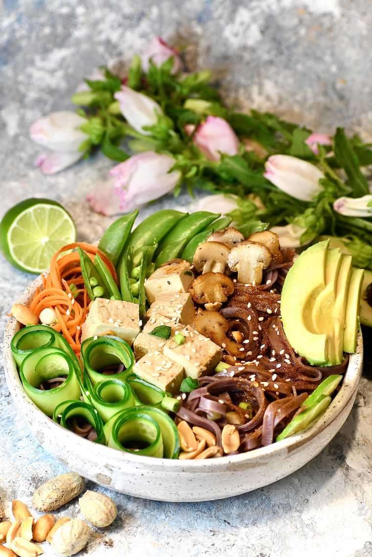 large white bowl with vegan sesame noodle bowl with avocado, spiralized veggies and tofu