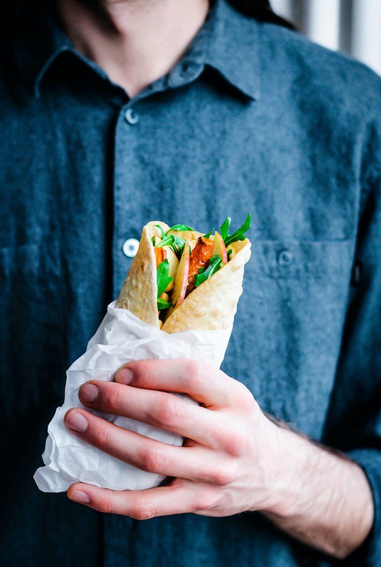 man in jeans shirt holding a colorful veggie-rich hummus wrap
