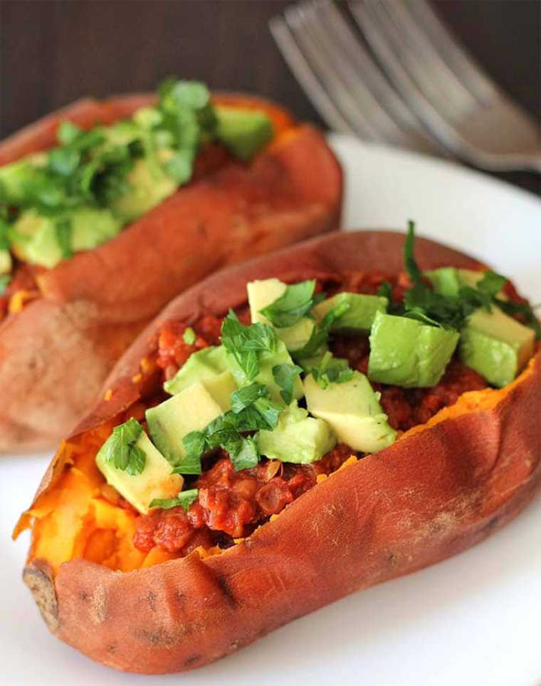 two baked and halved sweet potatoes filled with lentils and cubed avocado