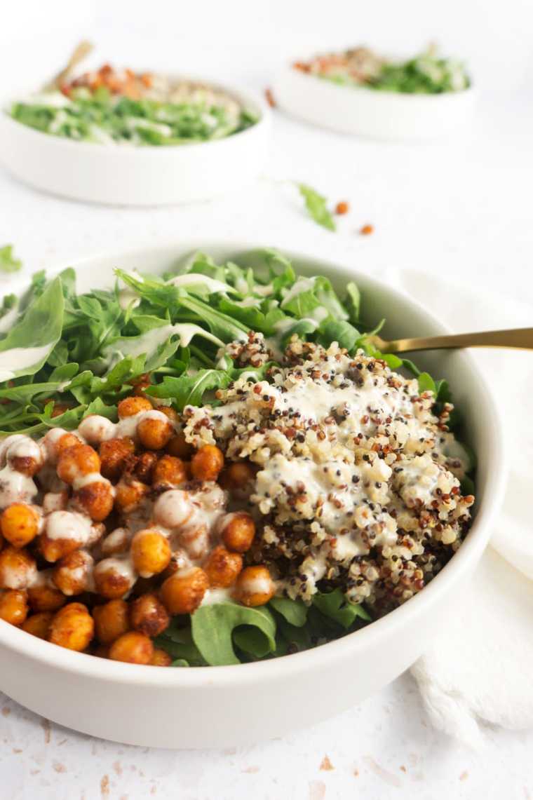 large white bowl with leafy greens, quinoa, chickpeas and sauce