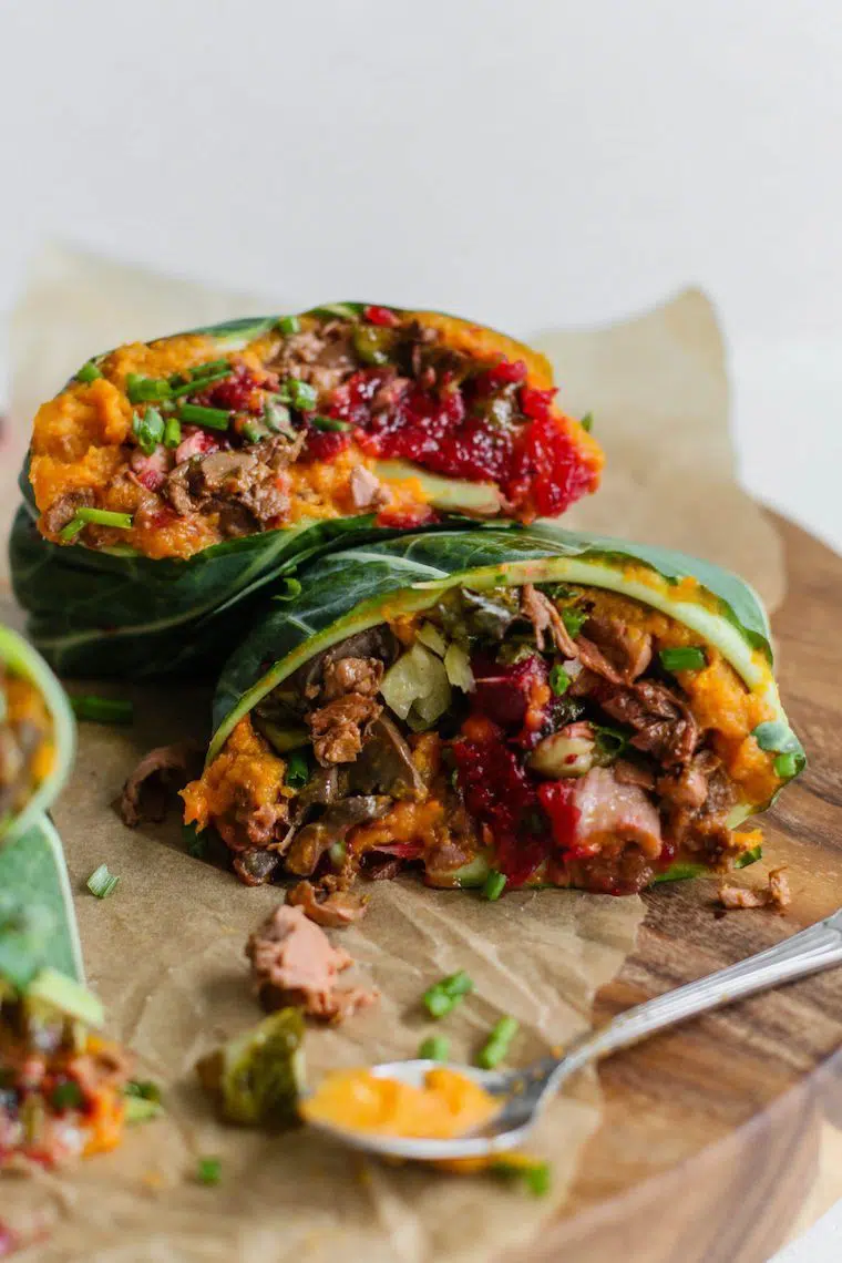 two colorfully stuffed vegan collard wraps on some parchment paper on a wooden chopping board