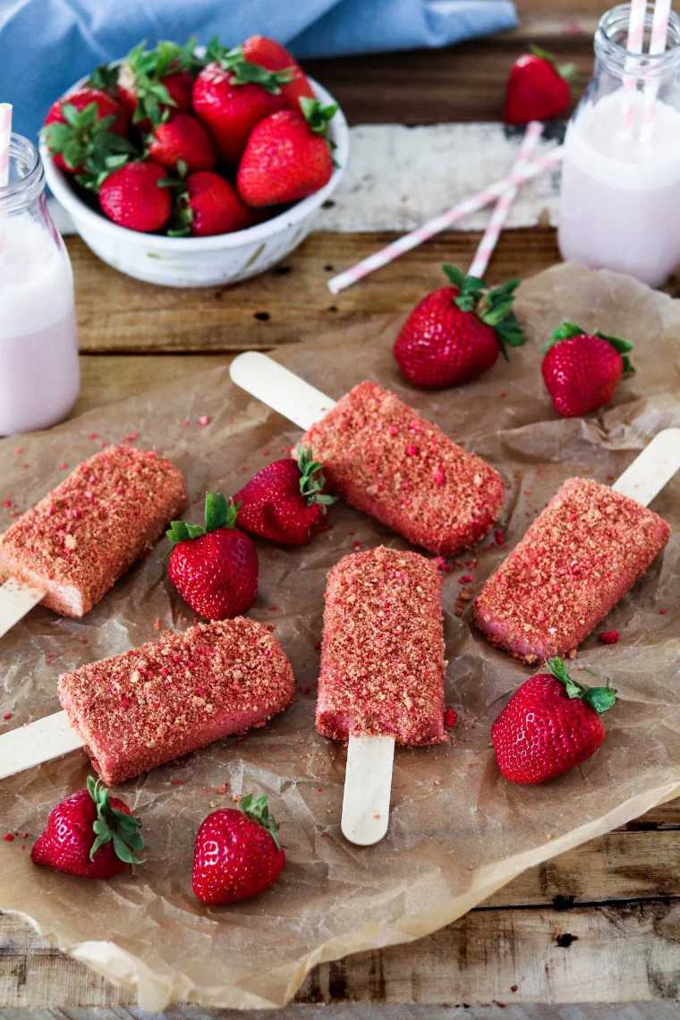 wooden table with fresh strawberries, parchment paper and five vegan Strawberry Shortcake Ice Cream Bars