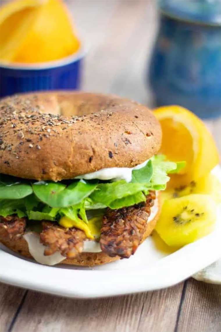 white plate with a vegan tempeh and lettuce bagel