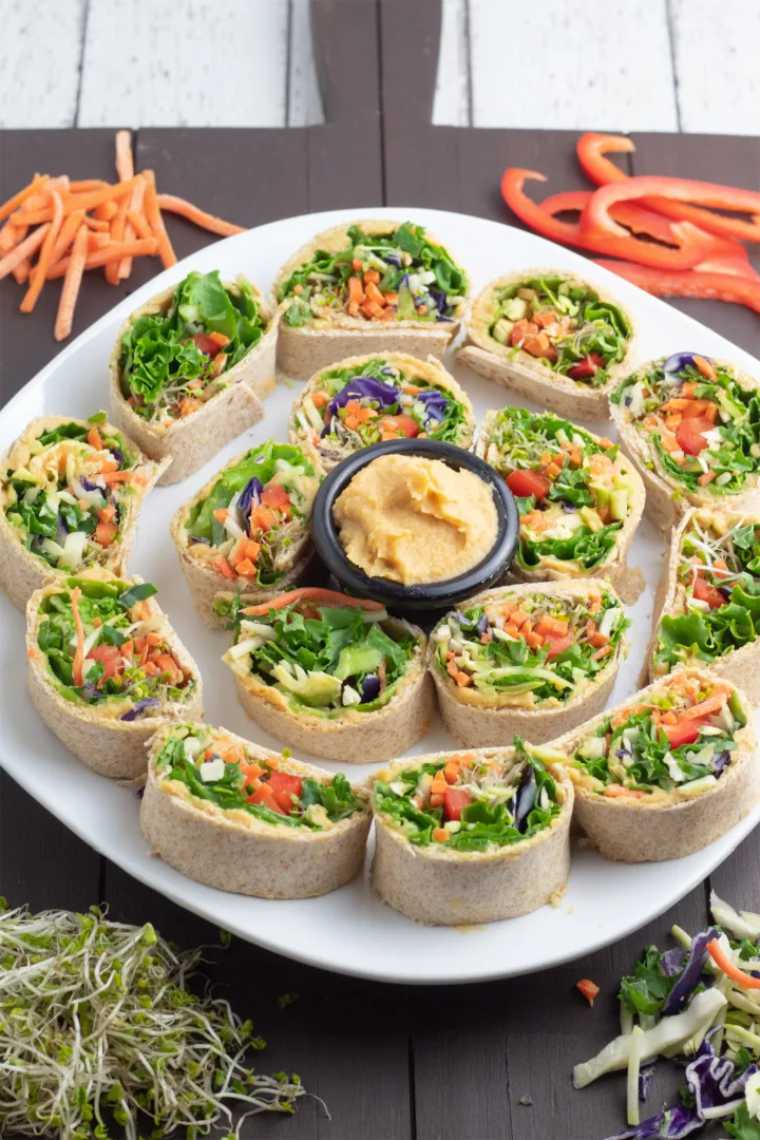 white plate with over a dozen of little vegan Sandwich Pinwheels and a dip